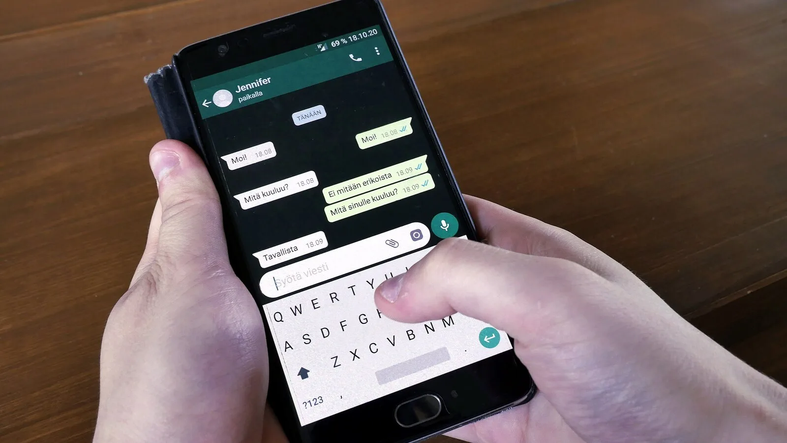 Duas mãos seguram um telemóvel Android com uma conversa do WhatsApp aberta e o teclado no ecrã