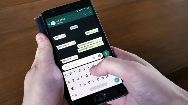 Duas mãos seguram um telemóvel Android com uma conversa do WhatsApp aberta e o teclado no ecrã