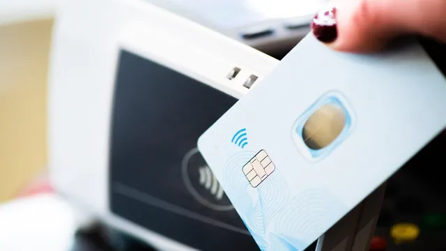 Mão a aproximar um cartão bancário branco, com chip, de um terminal de pagamento