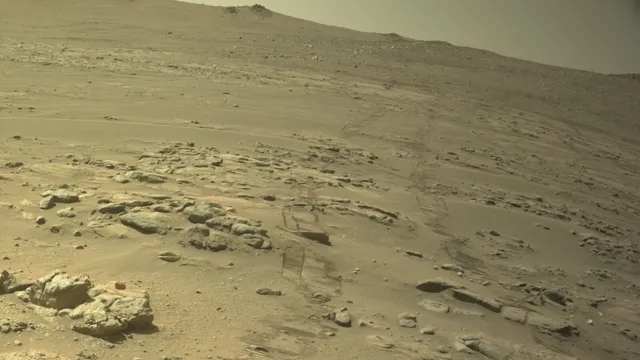 Terreno marciano arenoso e rochoso, com marcas de rodas, visto por uma câmara de navegação do rover Perseverance