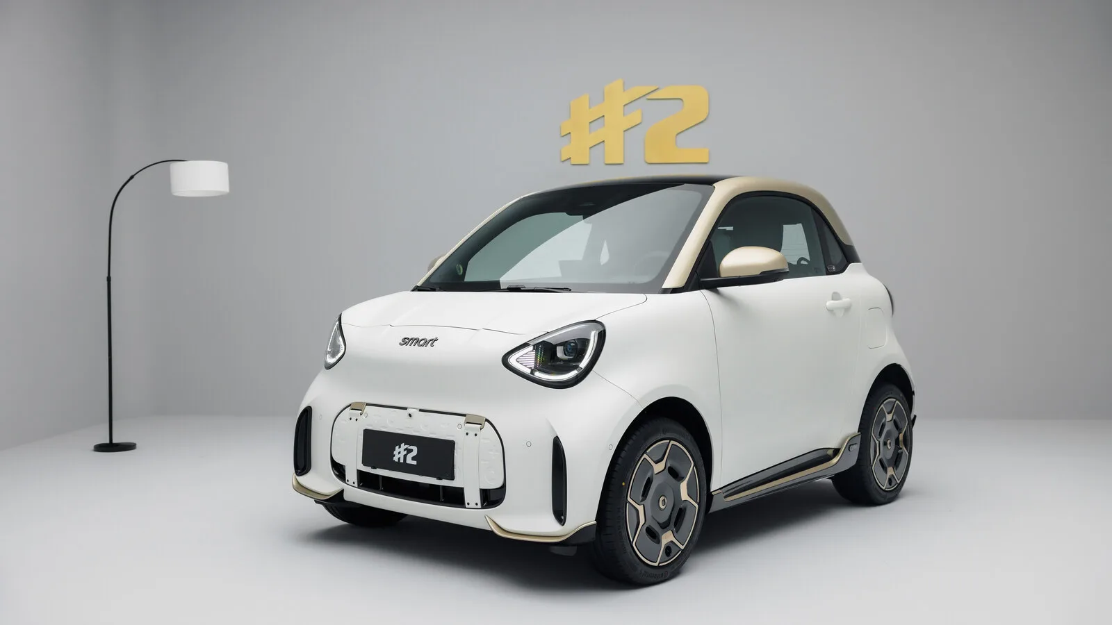 smart #2 Couture Edition branco mate com tejadilho dourado, visto de frente a três quartos num estúdio cinzento