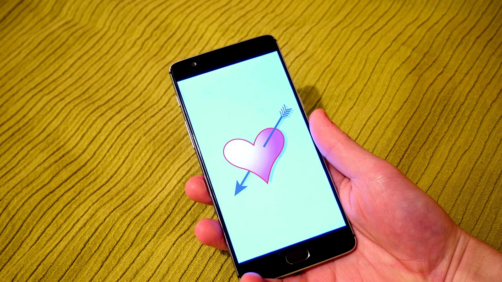 Mão a segurar um telemóvel com o desenho de um coração atravessado por uma seta no ecrã