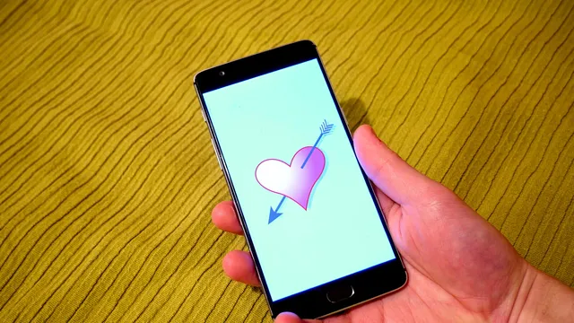 Mão a segurar um telemóvel com o desenho de um coração atravessado por uma seta no ecrã