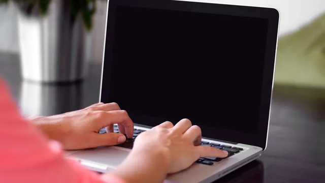 Mãos a escrever no teclado de um computador portátil com o ecrã escuro