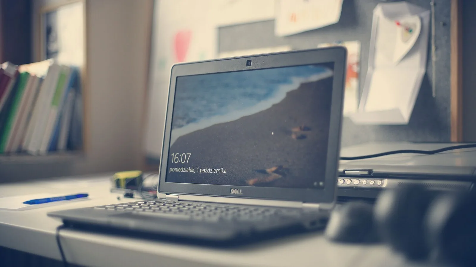 Portátil Dell aberto numa secretária, com o ecrã de bloqueio do Windows a mostrar as horas sobre uma fotografia de praia