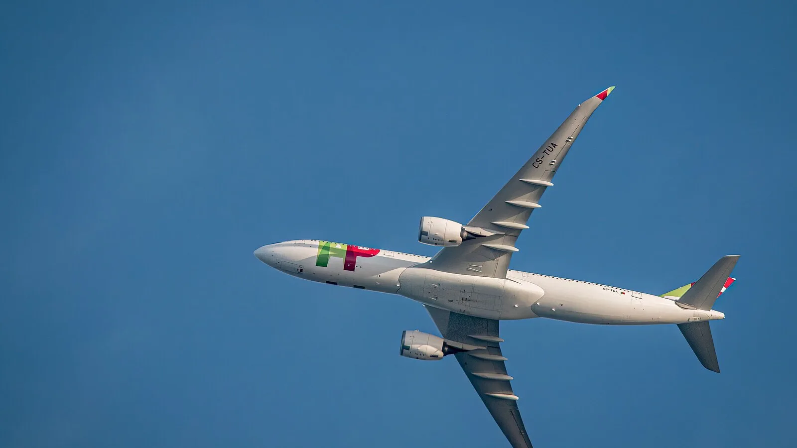 Avião da TAP Air Portugal em voo, visto de baixo, contra um céu azul sem nuvens