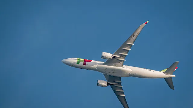 Avião da TAP Air Portugal em voo, visto de baixo, contra um céu azul sem nuvens