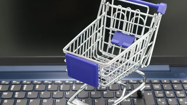 Carrinho de compras em miniatura, metálico e com detalhes azuis, pousado sobre o teclado de um computador portátil