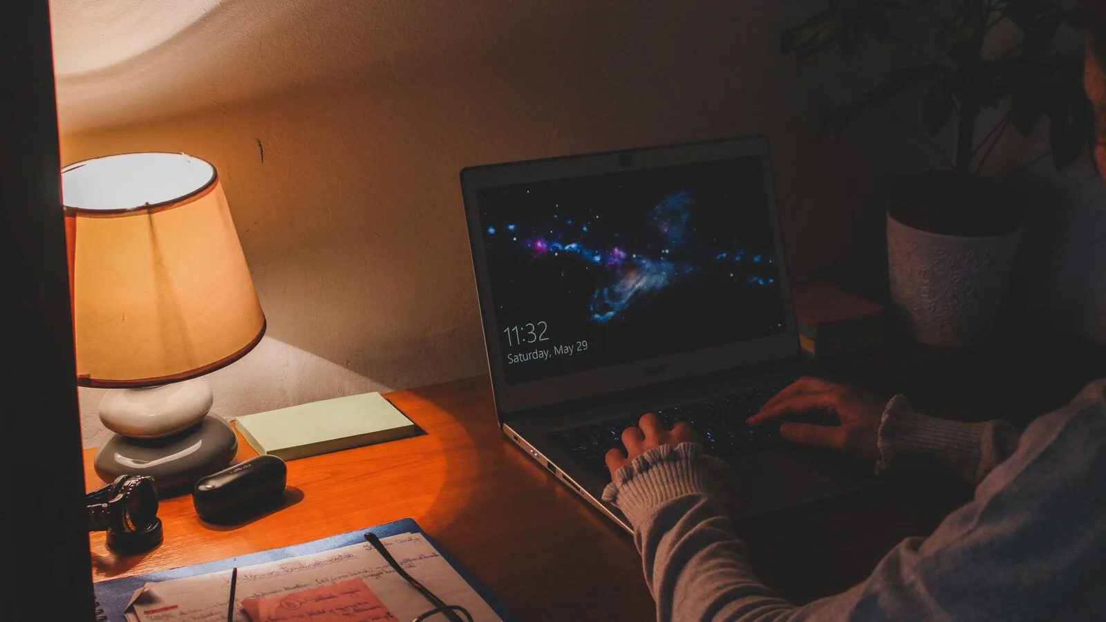 Pessoa a escrever num portátil com o ecrã de bloqueio do Windows, numa secretária iluminada por um candeeiro