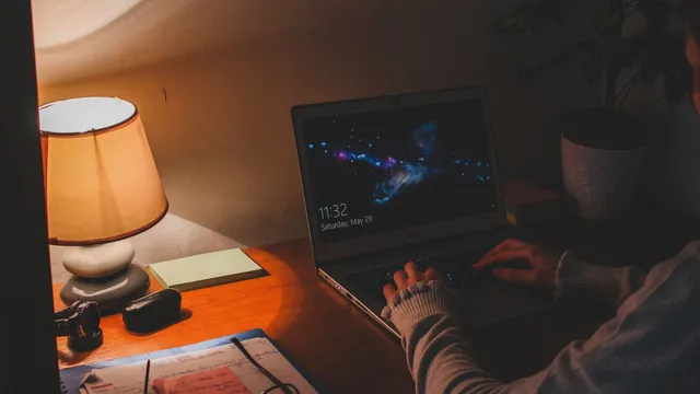 Pessoa a escrever num portátil com o ecrã de bloqueio do Windows, numa secretária iluminada por um candeeiro