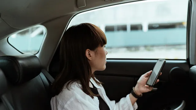Mulher sentada no banco de trás de um carro, a olhar pela janela com o telemóvel na mão