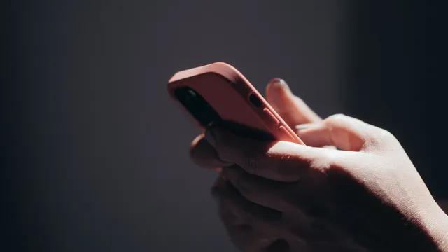 Mão a segurar um telemóvel com capa cor-de-rosa, sobre um fundo escuro
